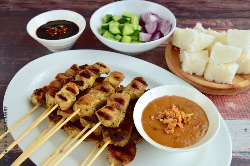 Indonesian chicken satay or Sate Ayam with lontong. Served with sweet soy sauce, peanut sauce and pickles cucumber and onion Indonesian chicken satay or Sate Ayam with lontong. Served with sweet soy sauce, peanut sauce and pickles cucumber and onion