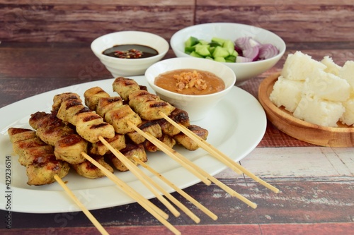 Indonesian chicken satay or Sate Ayam  with lontong. Served with sweet soy sauce, peanut sauce and pickles cucumber and onion