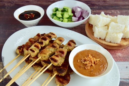Indonesian chicken satay or Sate Ayam with lontong. Served with sweet soy sauce, peanut sauce and pickles cucumber and onion
