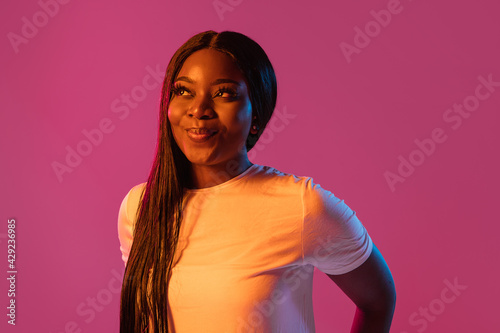 African young woman's portrait on pink studio background in neon. Concept of human emotions, facial expression, youth, sales, ad.