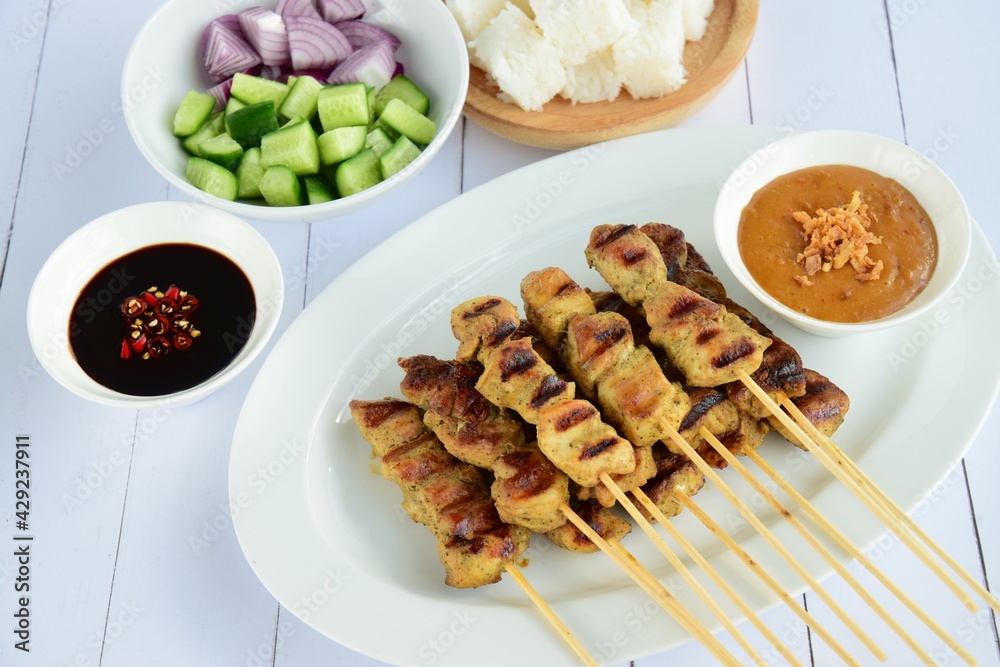 Indonesian chicken satay or Sate Ayam  with lontong. Served with sweet soy sauce, peanut sauce and pickles cucumber and onion