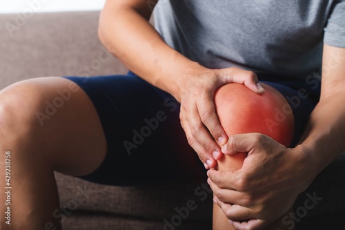 Image of a young man sitting on sofa holding his knees in pain.,Patellar tendon Inflammation.Healthcare and medical concept. photo