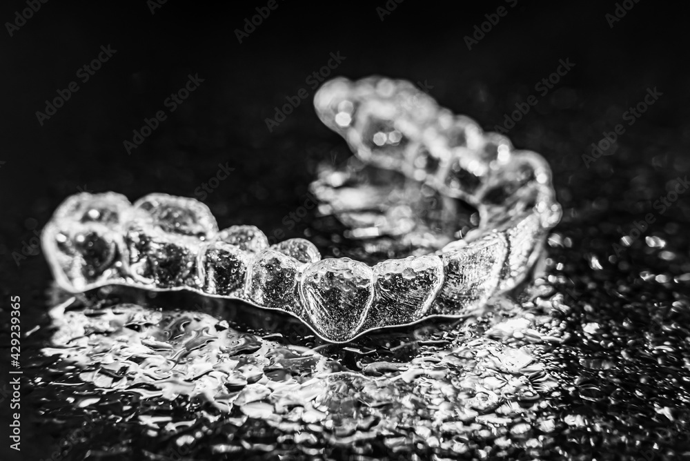 Transparent aligners, tooth retainers lie on a mirror with water droplets on a black background Transparent aligners, tooth retainers lie on a mirror with water droplets on a black background