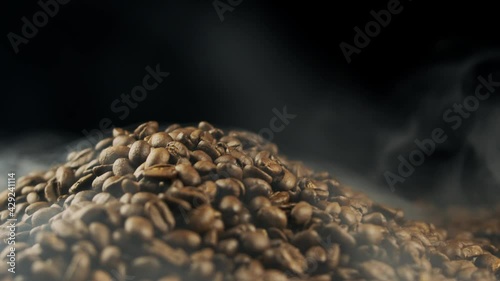 Close-Up Shot of Roasted Coffee Beans. Fragrant coffee beans are roasted smoke comes from coffee beans. Slow motion. Rotating camera. Organic coffee seeds.