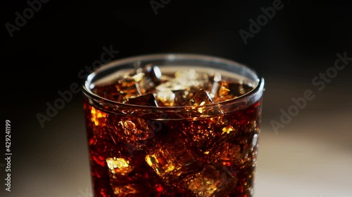 Cola with ice cubes close-up. Cola with Ice and bubbles in glass. Soda closeup. Food background. Rotate glass of Cola. Slow motion 4K  footage. Macro Shot.