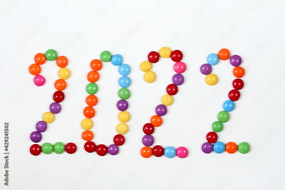 2022, colorful smarties on white background. Chocolate candies in shape of buttons, top view.