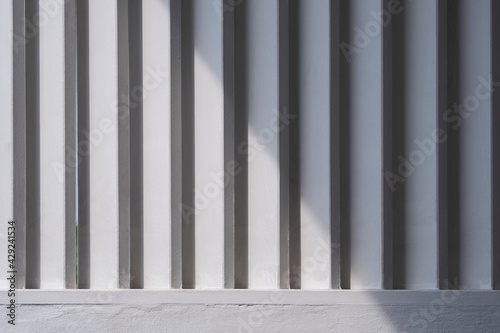White wooden sunshade battens on cement wall with sunlight and shadow on surface