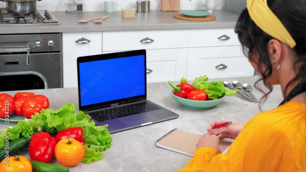 Blue screen mock up chroma key monitor laptop concept: Woman housewife in kitchen watch online cooking course listen teacher chef writes culinary recipe in notebook, study remote video call computer Blue screen mock up chroma key monitor laptop concept: Woman housewife in kitchen watch online cooking course listen teacher chef writes culinary recipe in notebook, study remote video call computer