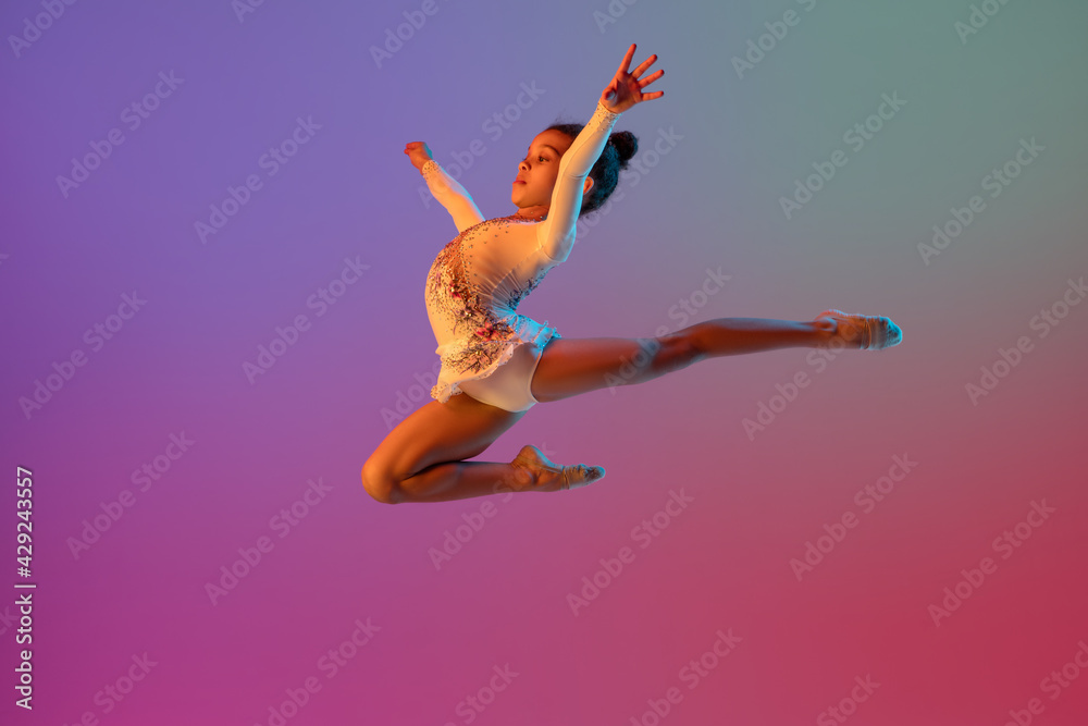 African-american rhythmic gymnast, pretty girl practicing on gradient studio background in neon light