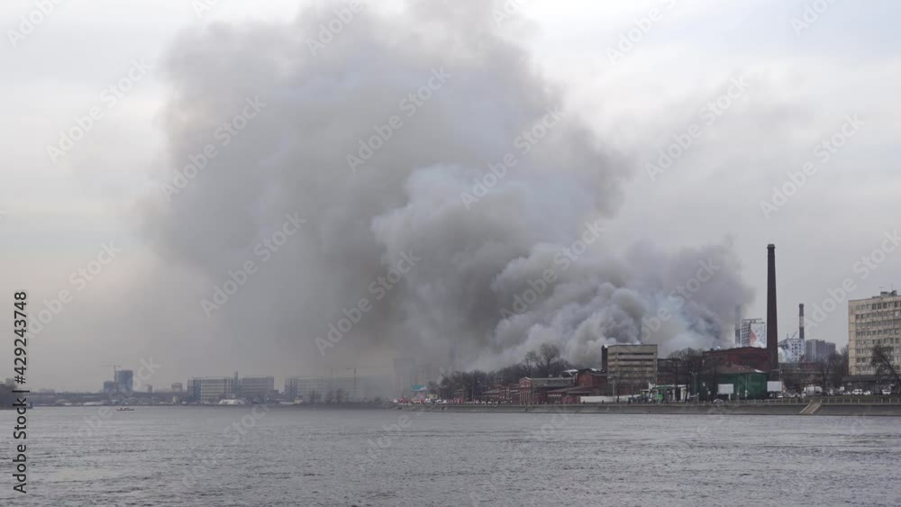 Fire. River embankment. Gray smoke rises. Fire trucks in the distance. Smoke is carried away into distance to residential areas Fire. River embankment. Gray smoke rises. Fire trucks in the distance. Smoke is carried away into distance to residential areas