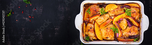 Baked chicken thighs. Appetizing slices of baked chicken with red onion and oranges in a baking dish. Top view, banner