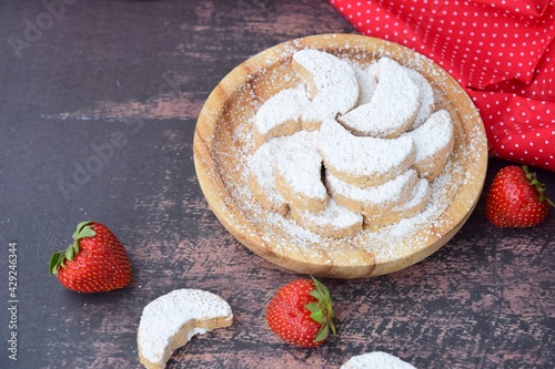 Putri Salju or crescent-shaped cookies coated with powdered sugar. Traditional Indonesian cookies to celebrate Eid al Fitr. Decorated with strawberries on wooden background photo