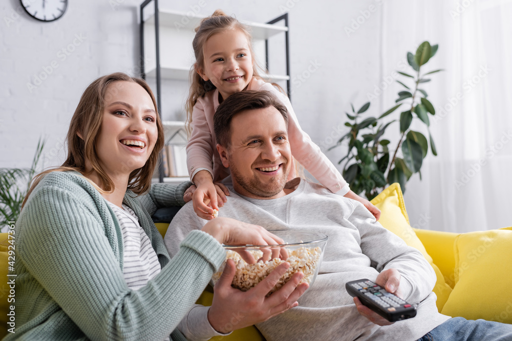 Smiling man holding remote controller and popcorn near family.