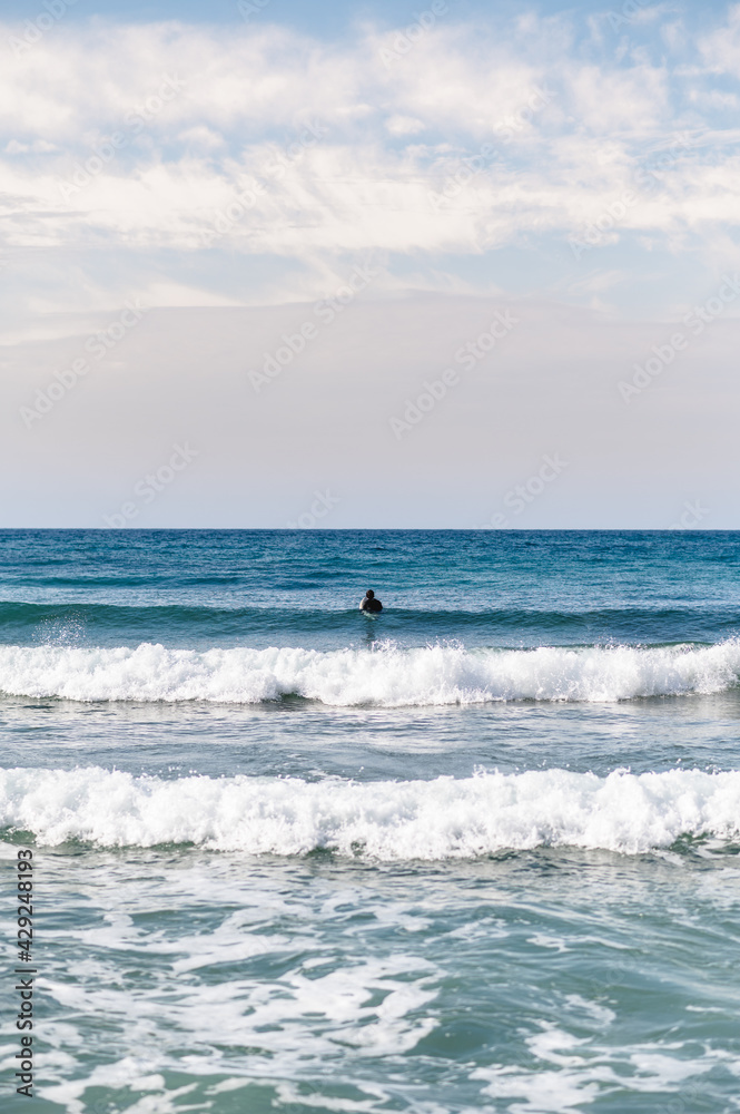 Unrecognizable surfer at distance with diving suit paddles hard waiting to catch the wave.