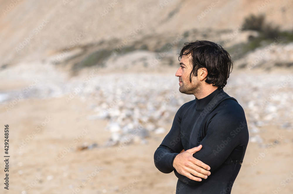 Side view medium shot wet man with diving suit and folded arms standing on the beach and looking at distance. Side view medium shot wet man with diving suit and folded arms standing on the beach and looking at distance.