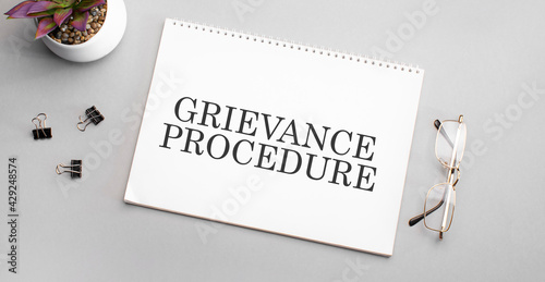 grievance procedure is written in a white notebook next to a pencil, black-framed glasses and a green plant. photo