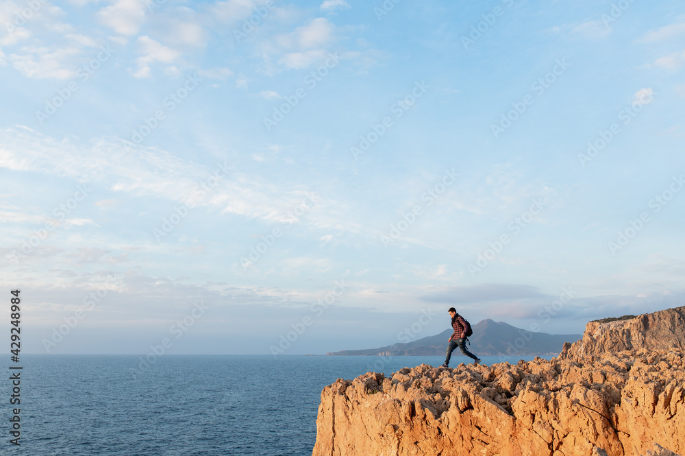 Fototapeta premium Young hiker man walking on a high jagged cliff overhanging the sea.