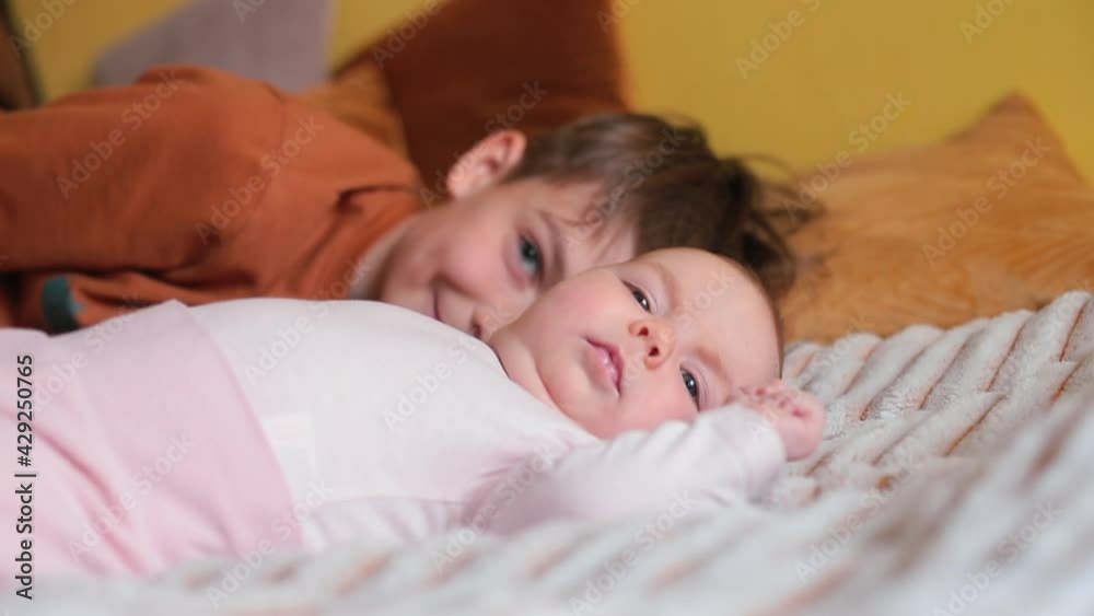 Teenager brother plays with his sister on the bed. The kid is lying. Lays his head affectionately, smiles. Family communication. Teenager brother plays with his sister on the bed. The kid is lying. Lays his head affectionately, smiles. Family communication.