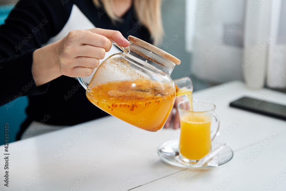 The girl pours sea buckthorn tea into a transparent cup. Close-up, selective focus