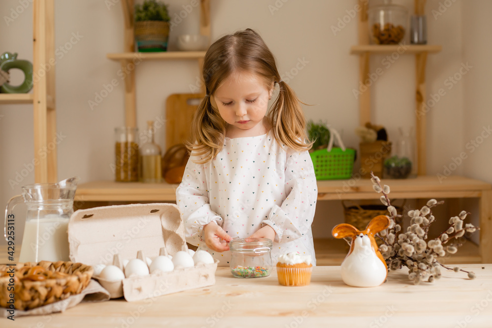 Cute little girl in a cotton dress at home in a wooden kitchen prepares an Easter cake Cute little girl in a cotton dress at home in a wooden kitchen prepares an Easter cake