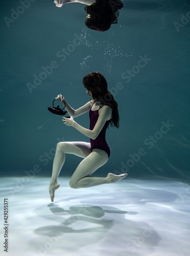 beautiful girl in a red swimsuit with a colored teapot and a cup is having a tea party under water on a blue background © константин константи