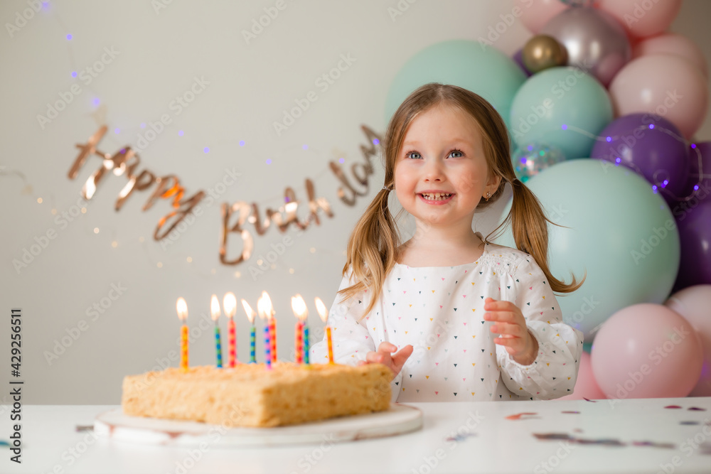 cute little girl blows out candles on a birthday cake at home against a ...