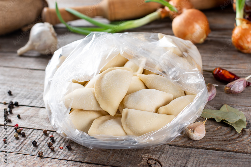 Traditional Russian dumplings, ravioli, meat dumplings on a wooden table. Rolling pin, napkin, garlic, onion, bay leaf and spices. Traditional Russian dumplings, ravioli, meat dumplings on a wooden table. Rolling pin, napkin, garlic, onion, bay leaf and spices.
