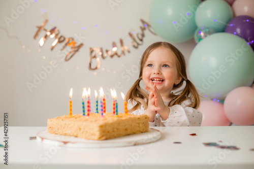 Photography cute little girl blows out candles on a birthday cake at home against a backdrop of balloons