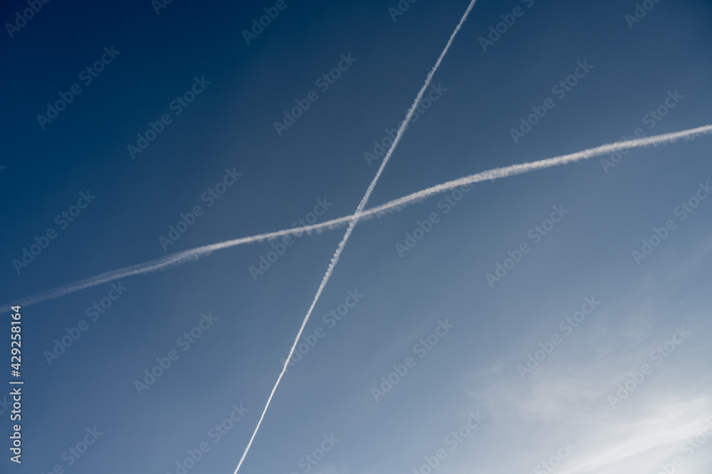 White trails, from jet exhaust, form a cross in the sky. A blue sky on the background White trails, from jet exhaust, form a cross in the sky. A blue sky on the background