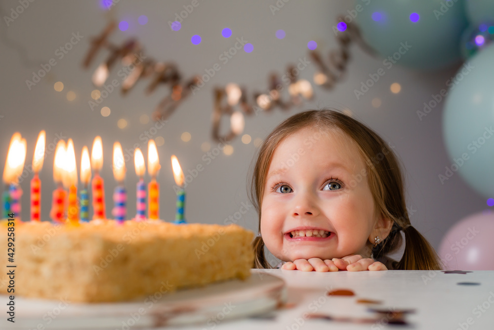 cute little girl blows out candles on a birthday cake at home against a