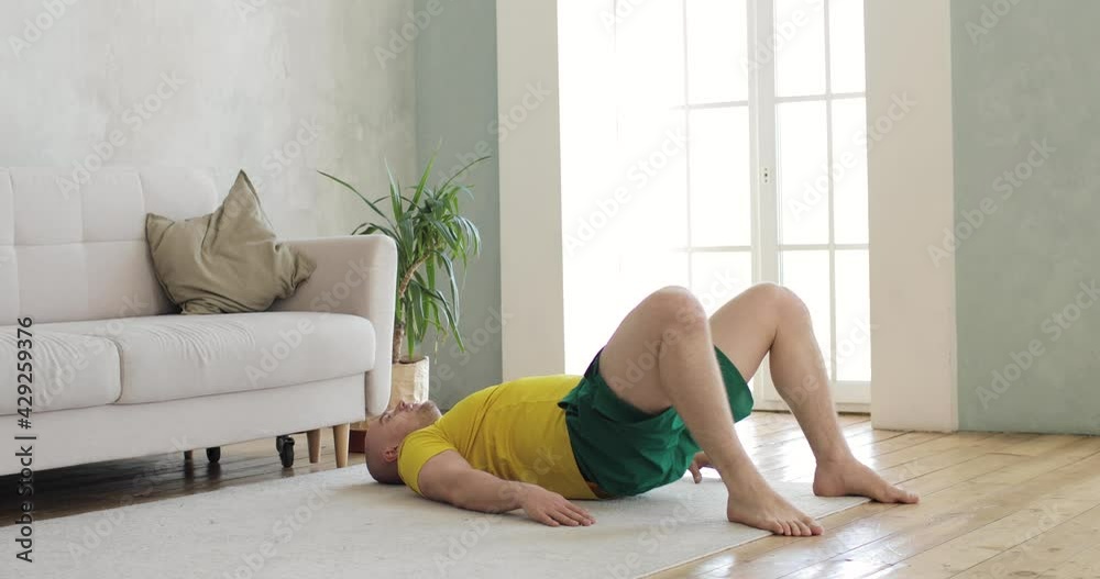 A young man works out at home against the background of a gray wall and a large window. Side view. A young man works out at home against the background of a gray wall and a large window. Side view.