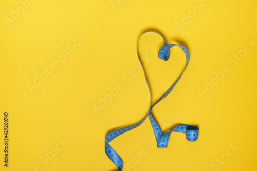 blue measuring tape in the form of heart on yellow background