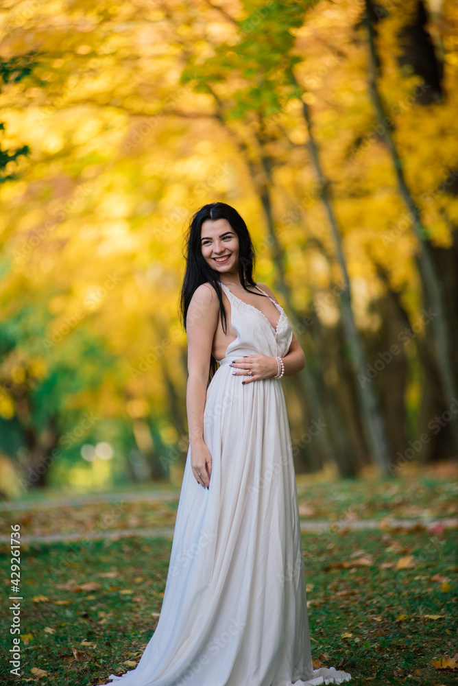 Beautiful brunette young female in white dress in autumn park Beautiful brunette young female in white dress in autumn park