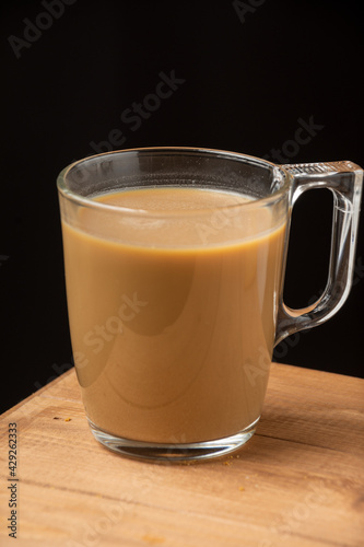 Close-up of glass cup of coffee with milk, on wooden table, dark background, vertical, with copy space