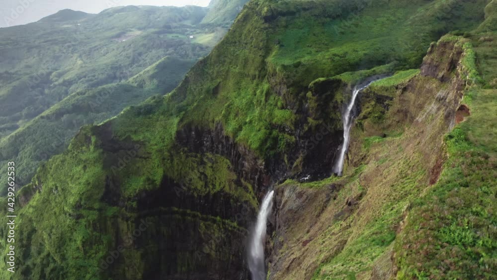 Top view of iconic waterfall of Poco Ribeira do Ferreiro, Alagoinha, Flores Island, Azores, Portugal, Europe. Drone shot of green mountain valley with falling water between rocks, 4k footage