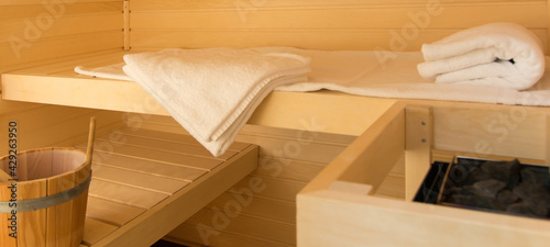 A small sauna with 2 wooden loungers. Small cabin in a bathroom. Sauna heater, loungers, water, towels.