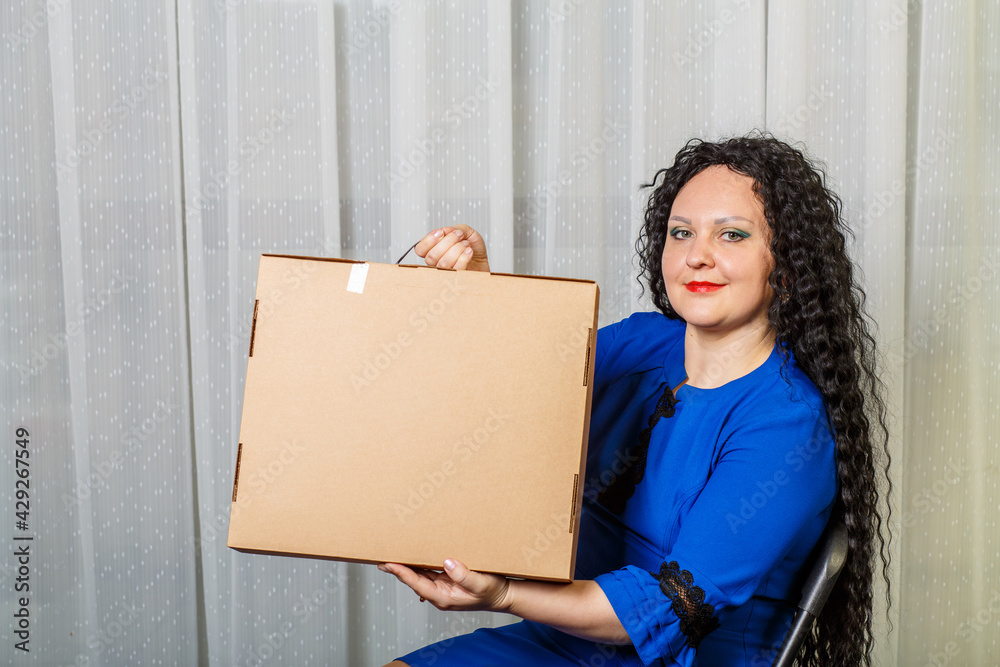 Curly joyful brunette woman holds in her hands a long-awaited purchase shows her. Curly joyful brunette woman holds in her hands a long-awaited purchase shows her.