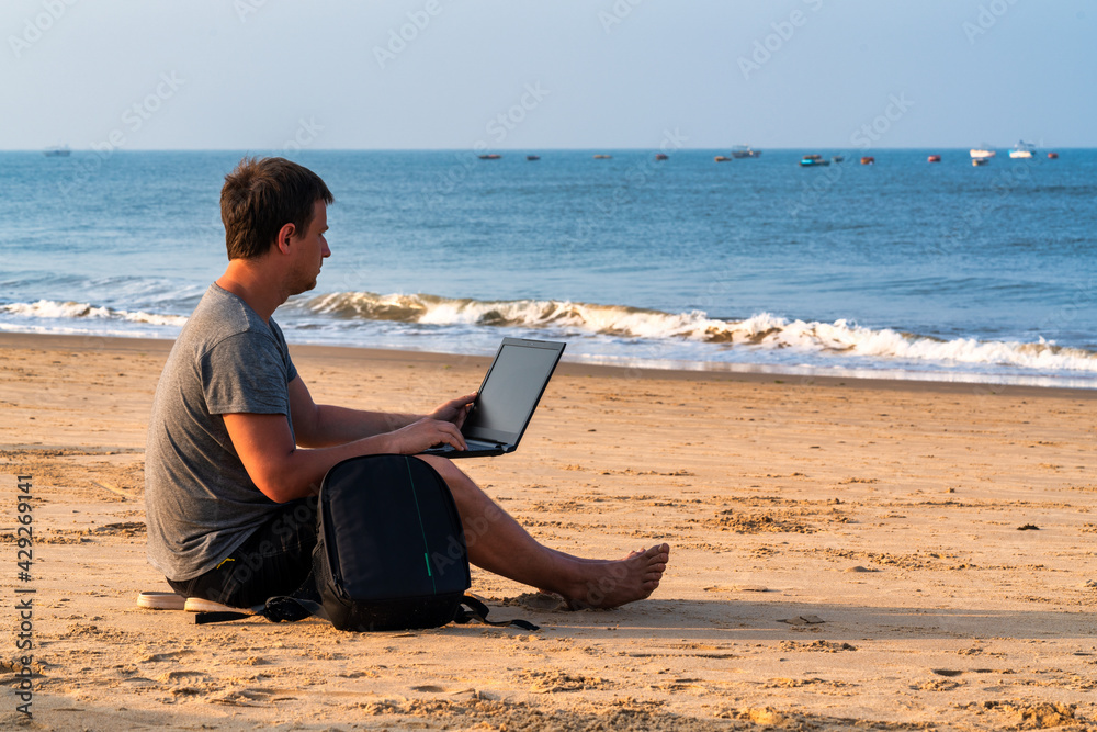 Young guy working on his laptop on the beach