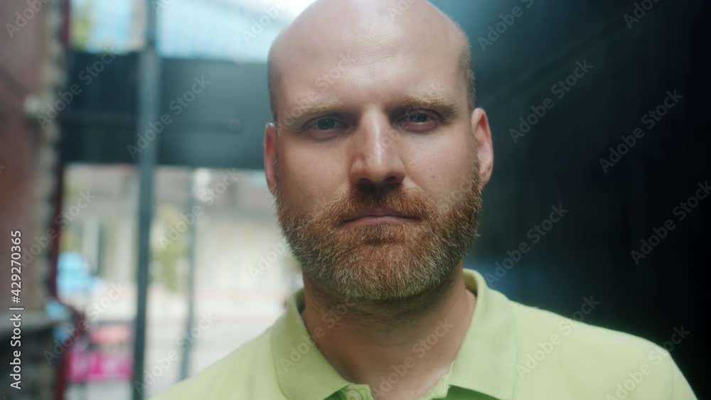 Close-up slow motion portrait of attractive bald guy with reddish beard standing outdoors in urban street and looking at camera with serious face Close-up slow motion portrait of attractive bald guy with reddish beard standing outdoors in urban street and looking at camera with serious face
