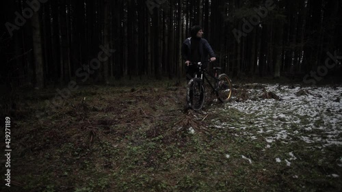 The guy is walking with a bike in the woods.