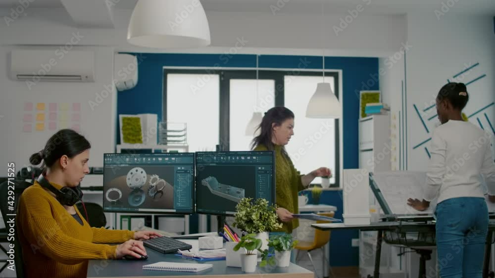 Industrial engineer putting on headset using pc with two monitors, screens showing CAD software with 3D Prototype of gears metalic mechanical piece. Employee working in creative agency office Industrial engineer putting on headset using pc with two monitors, screens showing CAD software with 3D Prototype of gears metalic mechanical piece. Employee working in creative agency office