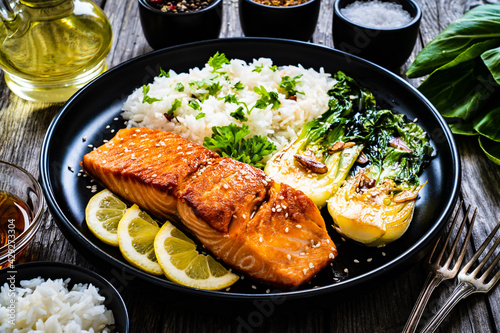 Fried salmon steak with lemon, jasmine rice and fried pak choi cabbage served on wooden table 