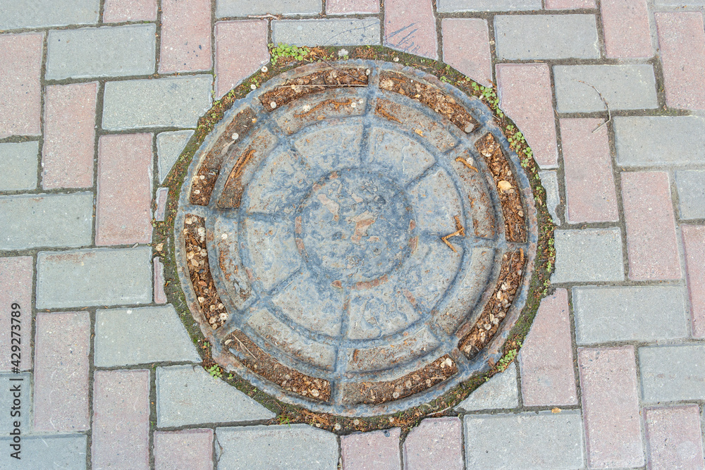 Old iron shabby sewer hatch embedded in the paving stones
