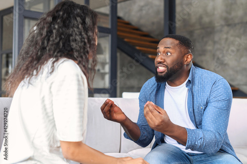 Irritated black guy screaming at the woman, angry boyfriend arguing and gesturing with annoyed face expression, African-American couple quarrels sitting on the couch at home