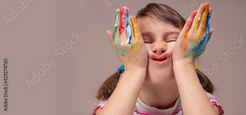 Portrait of beautiful young girl with colorful painted hands. Funny facial expression. Free space for text or design.