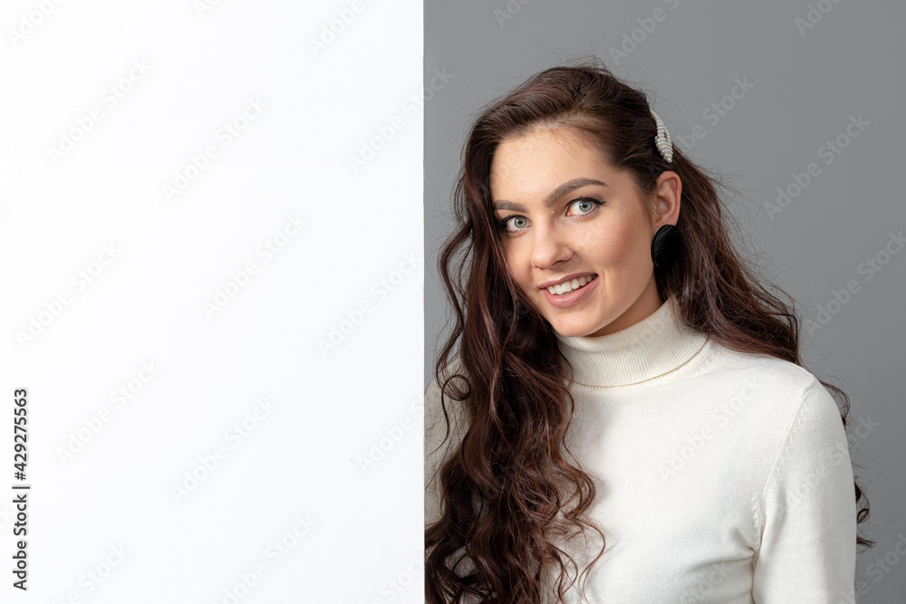 beautiful sensual woman with long curly hair shows a blank banner, isolated on gray, copy space beautiful sensual woman with long curly hair shows a blank banner, isolated on gray, copy space