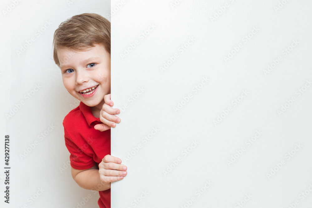 Funny child boy hiding behind blank white advertising billboard with copy space and peeking out Funny child boy hiding behind blank white advertising billboard with copy space and peeking out
