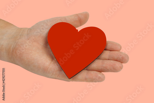 A man's hand holds his heart against a colored background.