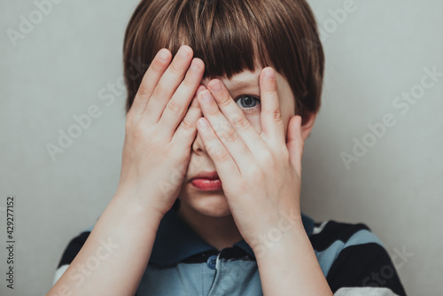 Unhappy kid boy hands hides his face, child mental health concept, world autism awareness day, teen autism spectrum disorder awareness concept