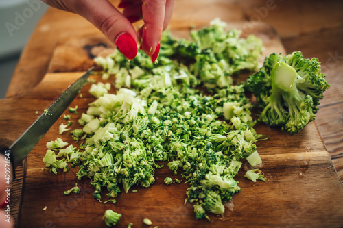 Closeup of a female chopping the fresh and tasty broccoli with a knife on a wooden cutting board